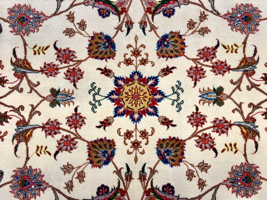 A close-up of an ornate floral patterned rug with a cream background and intricate motifs in red, blue, green, and brown.