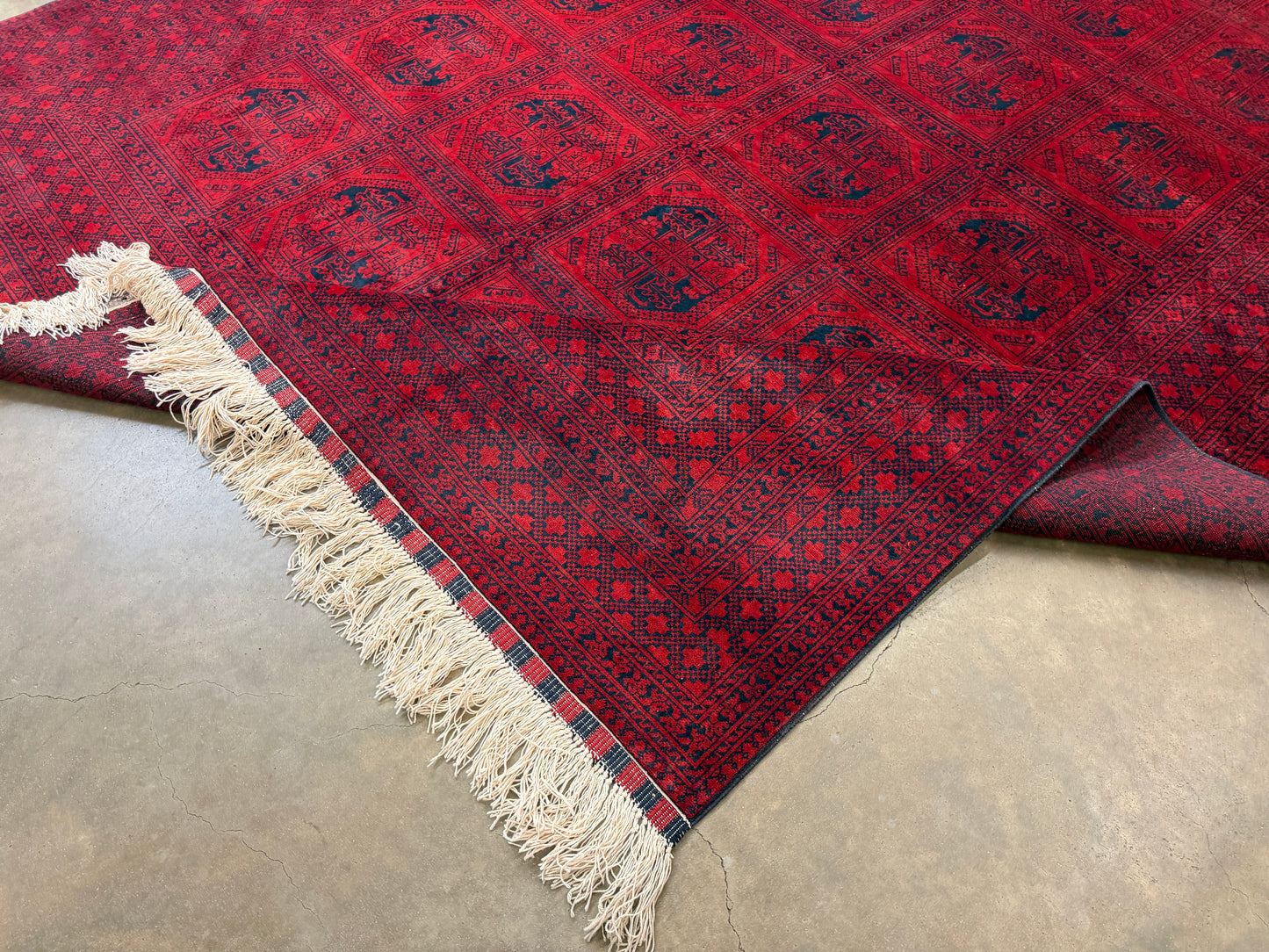 Red patterned rug with white fringe on a concrete floor