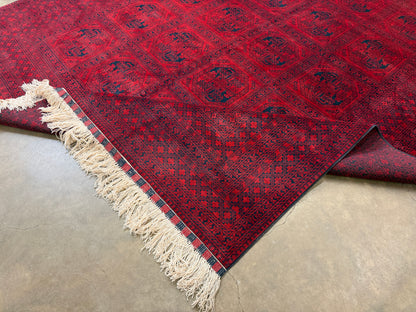 Red patterned rug with white fringe on a concrete floor