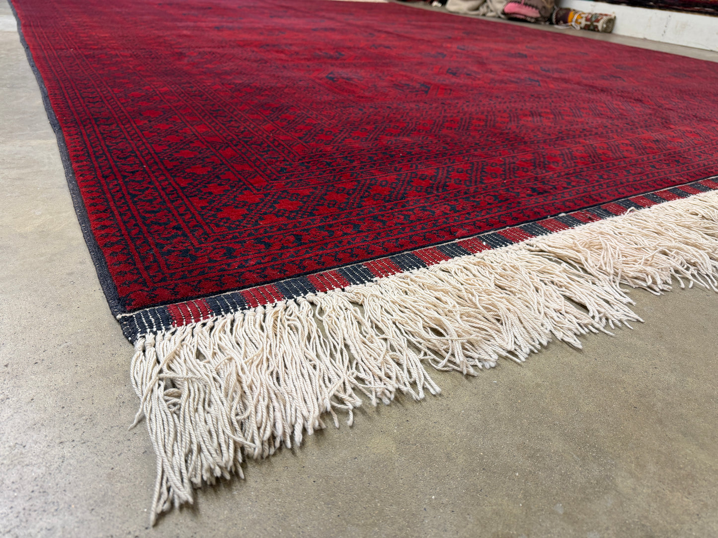 Red patterned rug with white fringe on a concrete floor