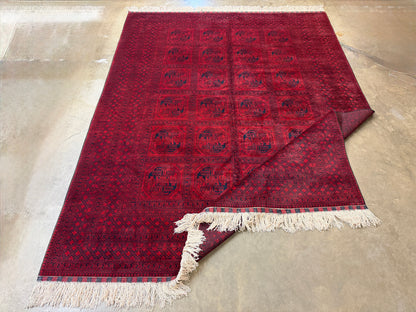 Red patterned rug with white fringe on a concrete floor