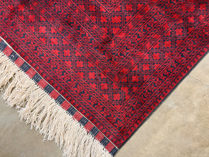 Red and black patterned rug with white fringe on a concrete floor
