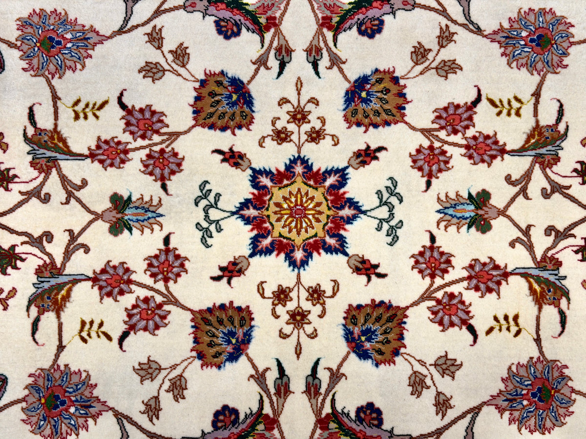 A close-up of an ornate floral patterned rug with a cream background and intricate motifs in red, blue, green, and brown.