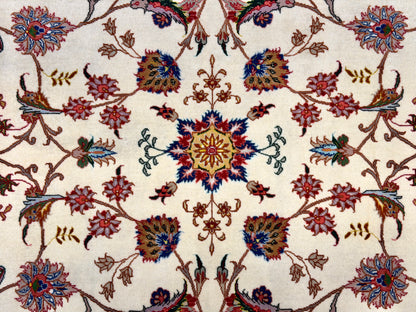 A close-up of an ornate floral patterned rug with a cream background and intricate motifs in red, blue, green, and brown.