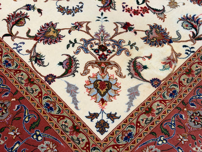 Close-up of an ornate area rug showing a cream field with a central floral medallion and a red border with detailed floral and geometric motifs.