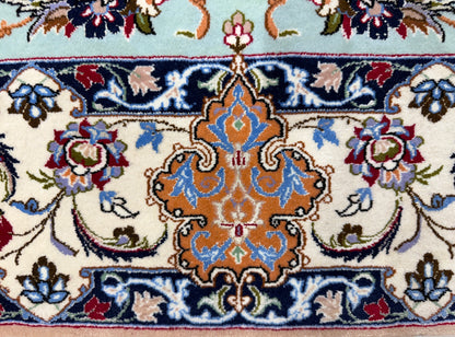 A close-up of a traditional patterned rug featuring a central ornate medallion in orange, blue, and cream, surrounded by floral motifs and bordered by navy and light blue sections.
