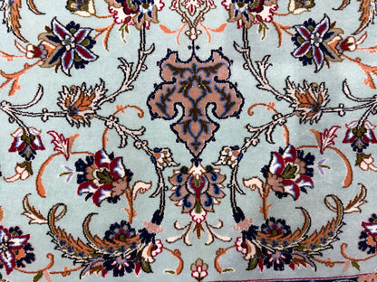 A close-up of an ornate floral patterned rug with a pale blue-green background and multicolored motifs in navy, burgundy, orange, beige, and gold.